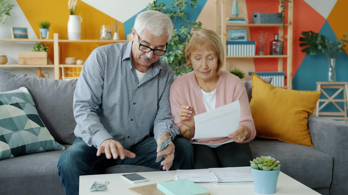 Älteres Ehepaar verwaltet Finanzen am Couchtisch.